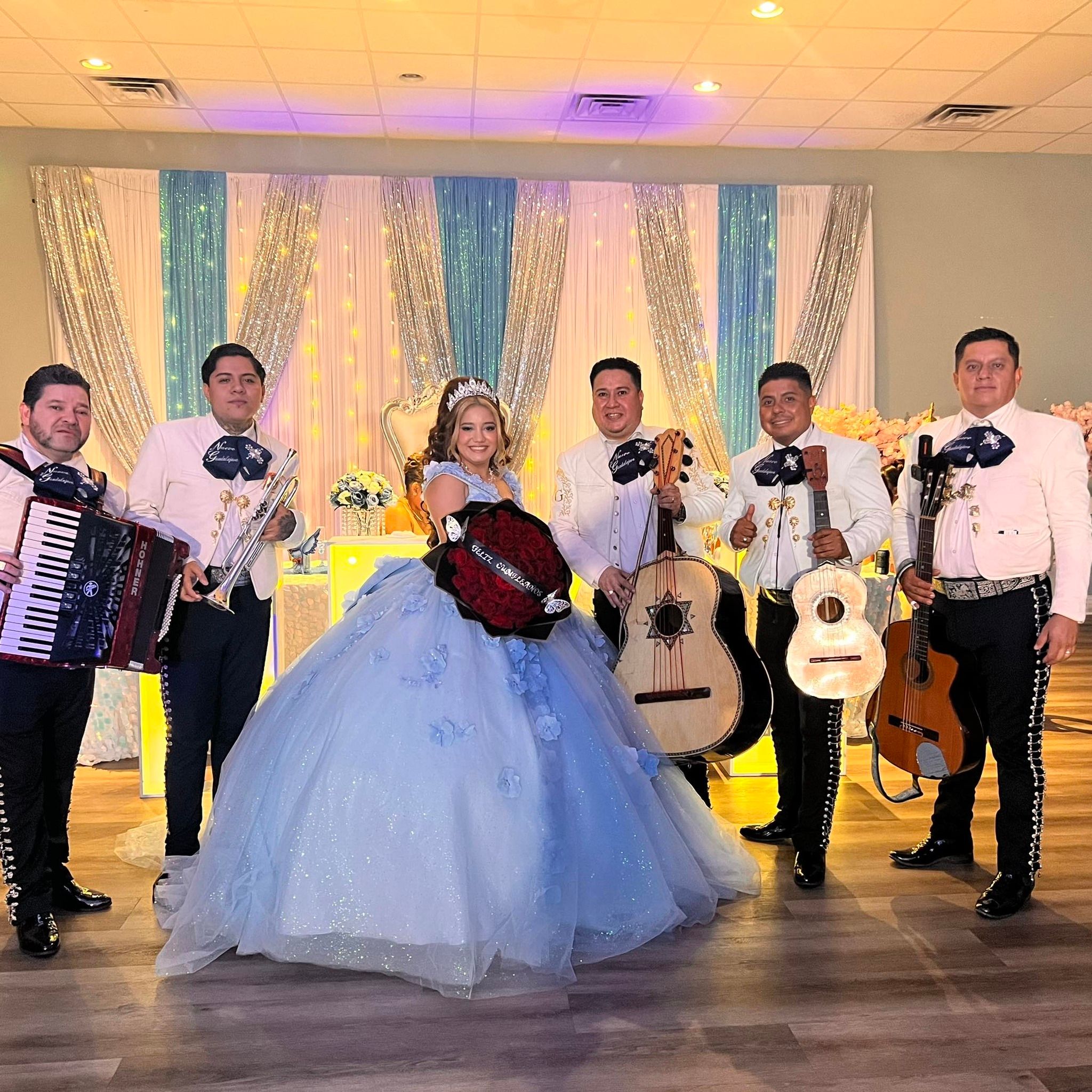 The mariachi stands with a quinceañera in a blue gown during a celebration.